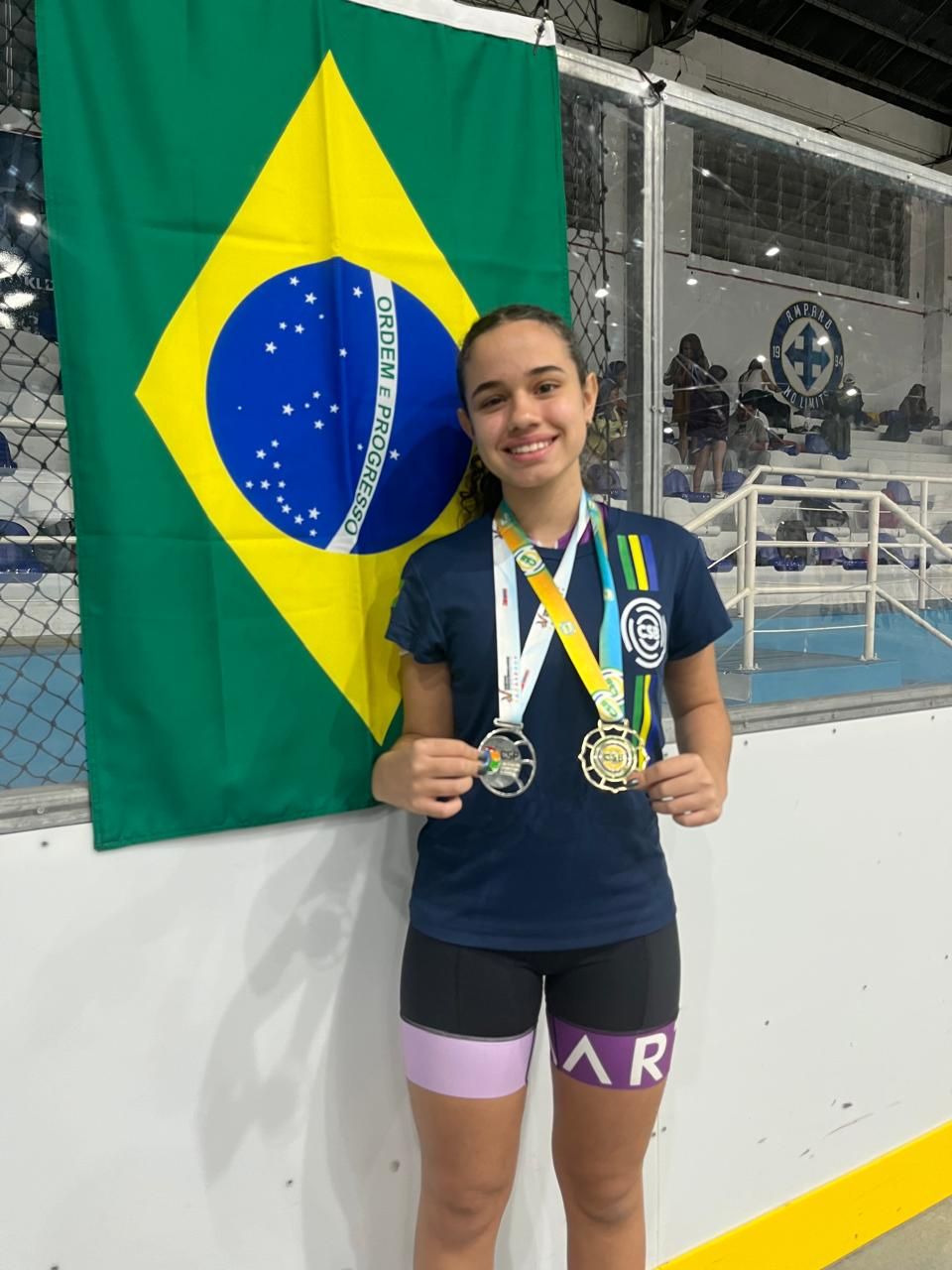 Yasmin com duas medalhas em frente à bandeira do Brasil