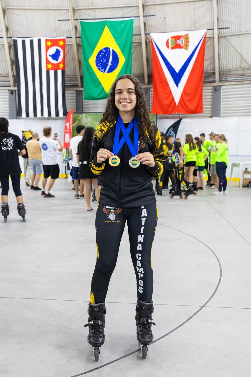 Yasmin com duas medalhas de ouro em frente às bandeiras do Brasil e de São Paulo