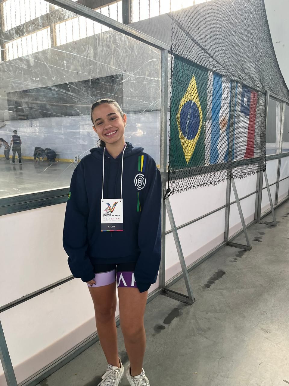 Yasmin sorrindo com a credencial no pescoço ao lado da pista
